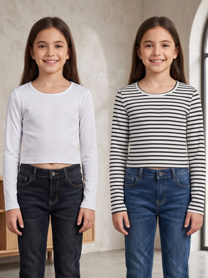 Two young girls standing side by side indoors, modeling long-sleeve crop tops. The girl on the left wears a plain white top with dark jeans, and the girl on the right wears a black-and-white striped top with blue jeans.