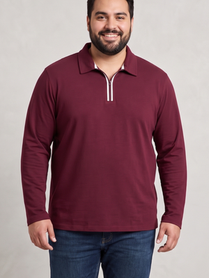 A man wearing a long-sleeve polo shirt in maroon with a white zipper trim, paired with blue jeans, standing against a light gray textured background.