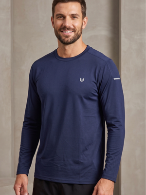 A man wearing a navy blue long-sleeve athletic shirt with a small white logo on the left chest, standing against a neutral textured beige wall.