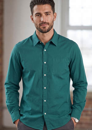 A man wearing a teal green long-sleeve button-down shirt with a chest pocket, standing in a softly lit indoor setting.