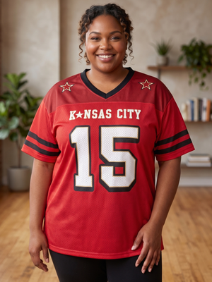 A smiling woman wearing a red Kansas City football-style jersey with black and white trim, the words 'KANSAS CITY' across the chest, and the number 15 on the front, standing in a softly lit indoor room with plants and shelves in the background.