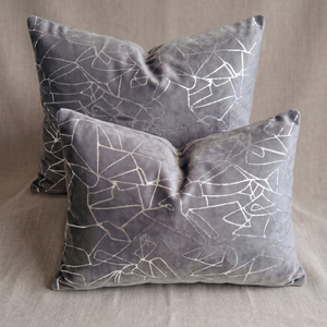 Two square gray velvet throw pillows with a white geometric line pattern, arranged on a neutral beige fabric background.