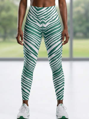 A model wearing high-waisted athletic leggings with a green and white diagonal striped pattern, paired with white sneakers, standing in front of a bright window.