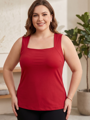 A smiling woman wearing a sleeveless red tank top with a square neckline and black leggings, standing in a bright indoor setting with a potted plant in the background.